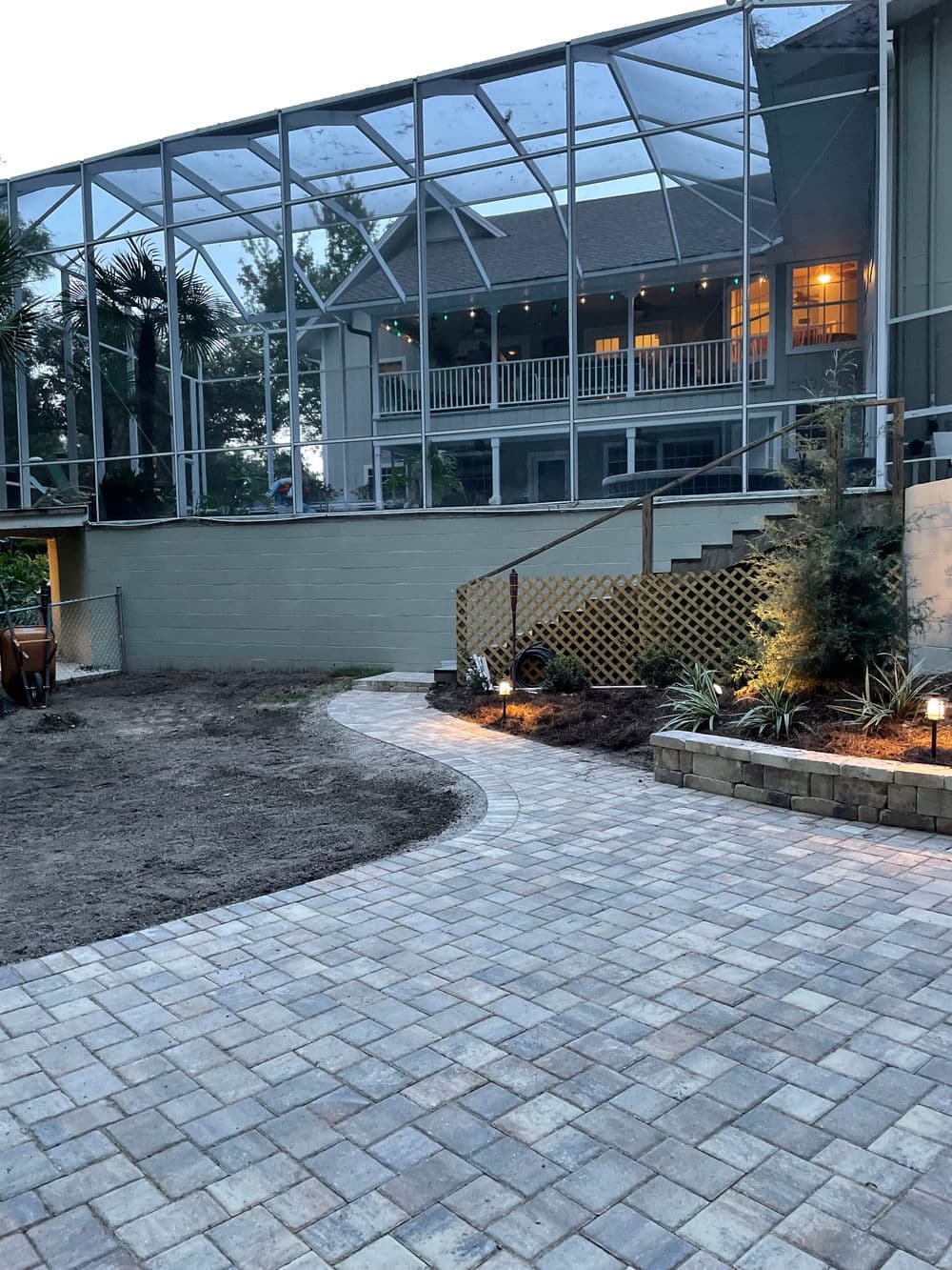 Paved walkway leading to a screened patio with evening lights and landscaped features.