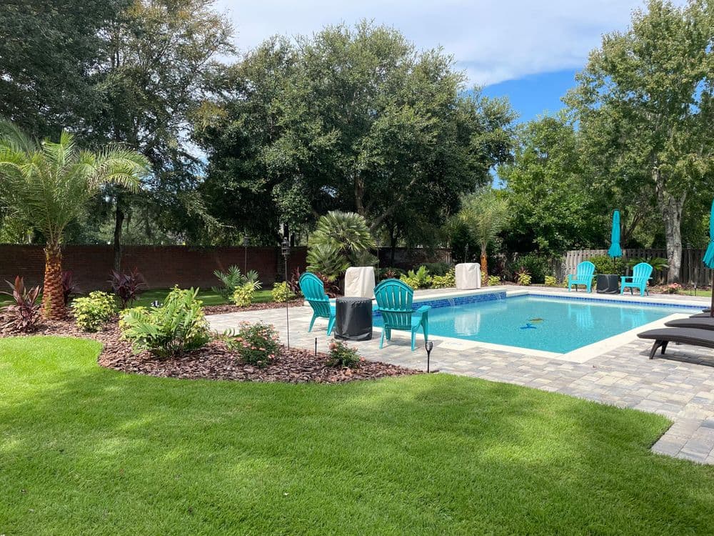 Inviting backyard with a pool, lounge chairs, palm trees, and vibrant landscaping.