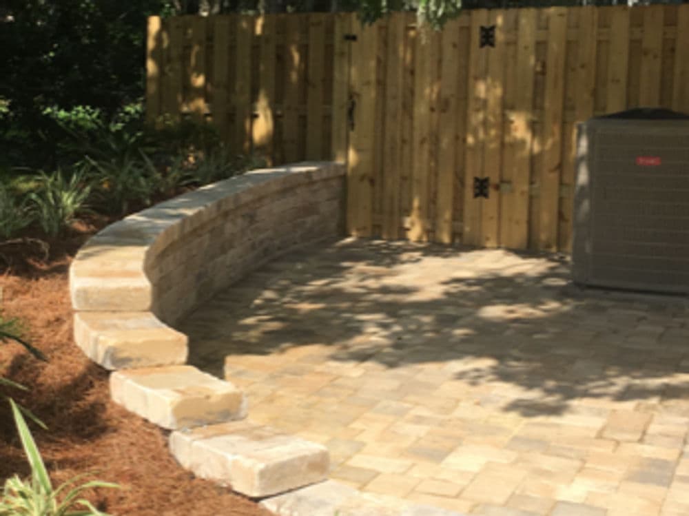 Curved stone seating area beside wooden fence and air conditioner unit.